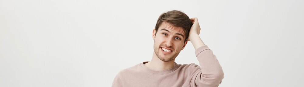 Jovem, de moletom de cor neutra, co&ccedil;ando o cabelo sugerindo a presen&ccedil;a de caspa