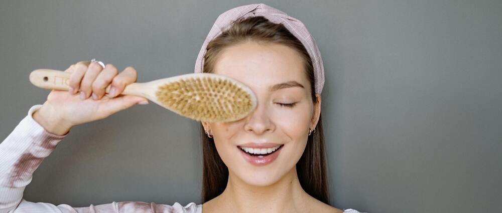 Mo&ccedil;a alegre segurando uma escova de cabelo utilizada para seus cuidados capilares