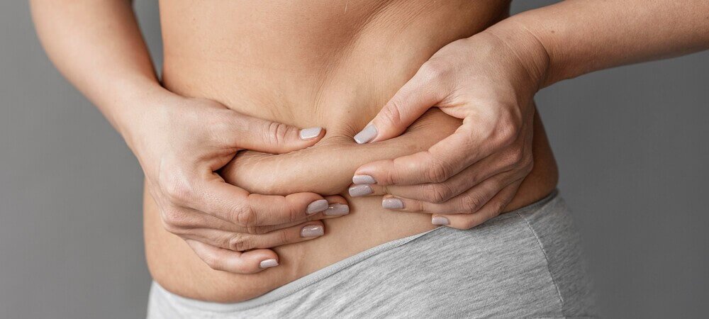 Mulher branca, com unhas de cor cinza, combinando com a roupa,apalpando seu excesso de gordura abdominal