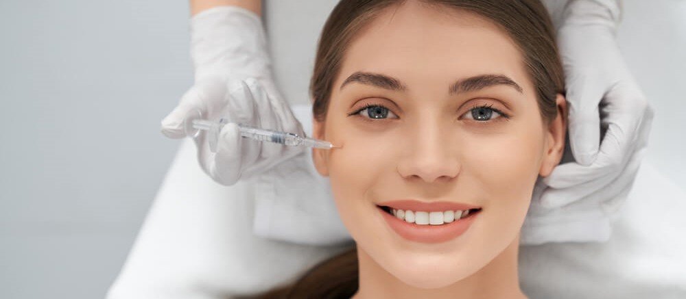 Mo&ccedil;a de cabelos castanhos sorridente aplicando uma inje&ccedil;&atilde;o para rejuvenescimento facial